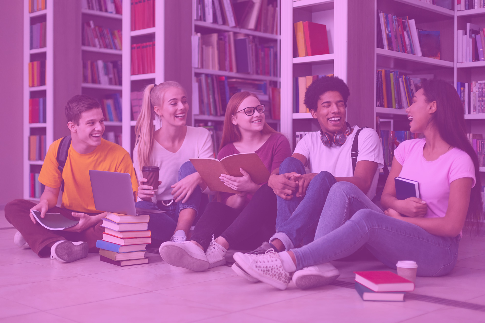 Eine Gruppe junger Menschen sitzt lachend vor Bücherregalen.